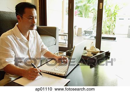 Stock Image - Man in living room, using laptop. Fotosearch