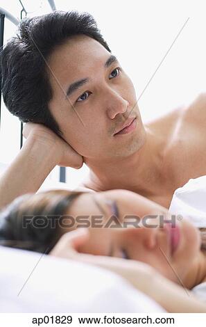 Stock Photo - Man leaning on hand, woman asleep next to him. Fotosearch