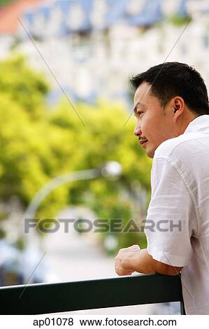 Stock Photo - Man leaning on railing, looking away. Fotosearch