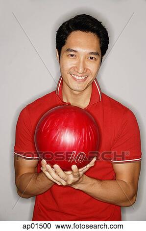 Stock Image - Man looking at camera, holding bowling ball. Fotosearch
