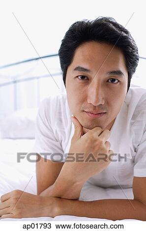 Man lying on bed, hand on chin, looking at camera View Large Photo Image Stock Image - Man lying on bed, hand on chin, looking at camera. Fotosearch