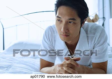 Stock Image - Man lying on bed, hands clasped. Fotosearch