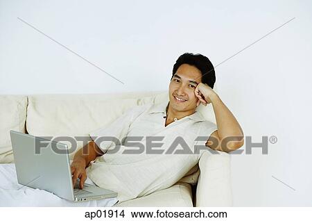 Man lying on sofa, using laptop, hand on head View Large Photo Image Picture - Man lying on sofa, using laptop, hand on head. Fotosearch