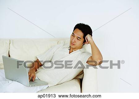 Man lying on sofa, using laptop View Large Photo Image Stock Image - Man lying on sofa, using laptop. Fotosearch