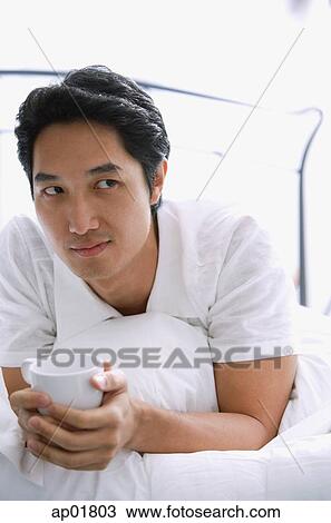 Man on bed, holding cup View Large Photo Image Stock Image - Man on bed, holding cup. Fotosearch