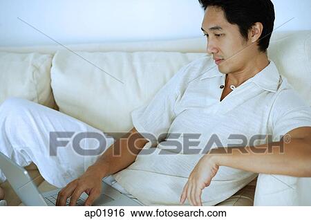 Man on sofa, using laptop View Large Photo Image Stock Photograph - Man on sofa, using laptop. Fotosearch