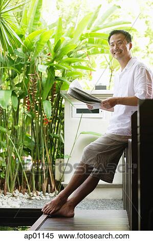 Man sitting, holding newspaper, looking at camera View Large Photo Image Stock Photography - Man sitting, holding newspaper, looking at camera. Fotosearch