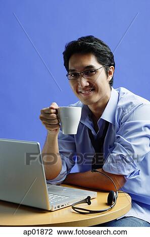 Man sitting in front of laptop, holding mug, smiling at camera View Large Photo Image Stock Image - Man sitting in front of laptop, holding mug, smiling at camera. Fotosearch