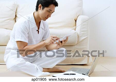 Stock Photography - Man sitting on floor, using laptop and calculator. Fotosearch