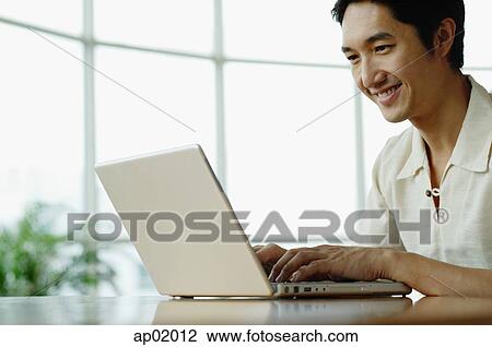 Stock Image - Man sitting, using laptop, smiling. Fotosearch