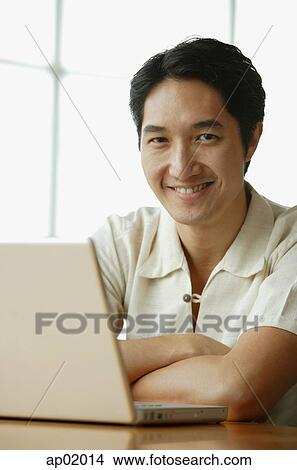 Man smiling at camera, laptop in front of him View Large Photo Image Picture - Man smiling at camera, laptop in front of him. Fotosearch