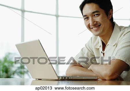 Stock Image - Man smiling at camera, laptop on table. Fotosearch