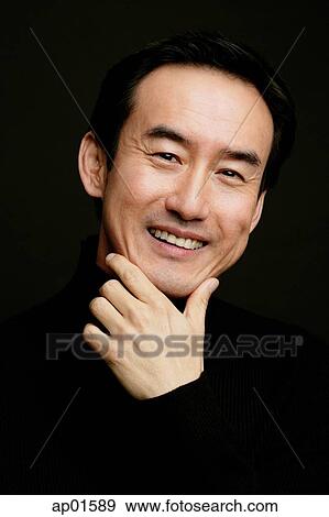 Stock Photo - Man smiling, head shot, hand on chin, black background. Fotosearch