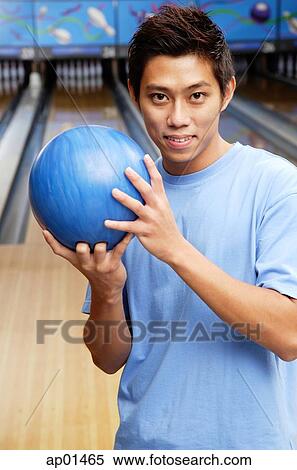 Stock Photography - Man standing in bowling ally, holding bowling ball, looking at camera. Fotosearch