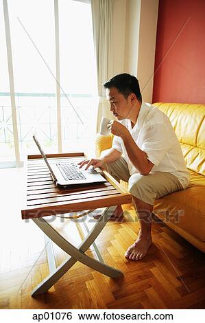 Man using laptop, drinking from mug View Large Photo Image Stock Photograph - Man using laptop, drinking from mug. Fotosearch