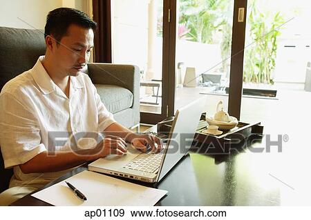 Man using laptop, in living room View Large Photo Image Stock Photo - Man using laptop, in living room. Fotosearch
