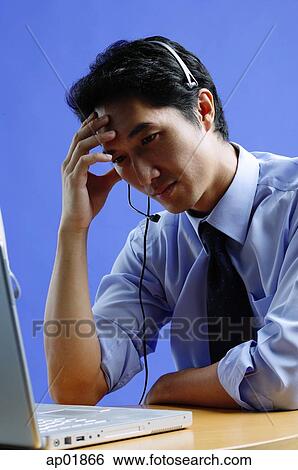 Man wearing headset, using laptop, hand on head View Large Photo Image Stock Photograph - Man wearing headset, using laptop, hand on head. Fotosearch