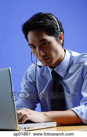 Man wearing headset, using laptop View Large Photo Image Stock Photo - Man wearing headset, using laptop. Fotosearch