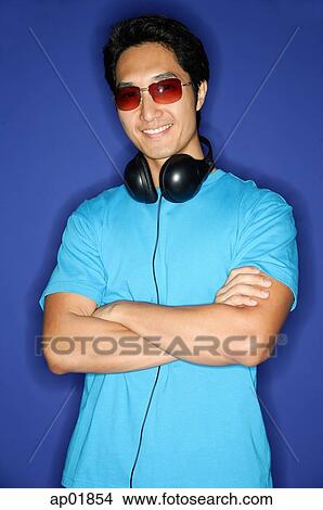 Picture - Man wearing sunglasses, headphones around his neck, arms crossed. Fotosearch