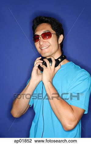 Stock Image - Man wearing sunglasses, headphones around his neck. Fotosearch
