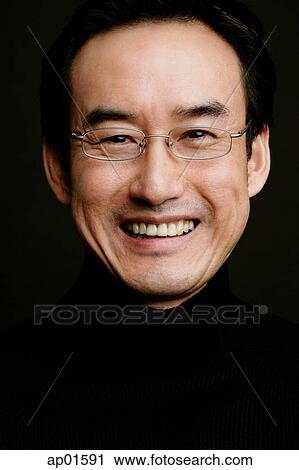 Stock Image - Man with glasses, smiling, head shot, black background. Fotosearch
