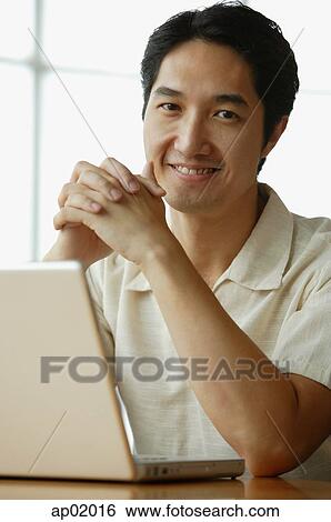 Stock Photograph - Man with laptop, leaning elbows on table, hands clasped. Fotosearch