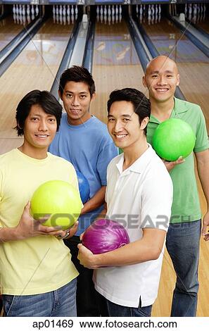Stock Photo - Men in bowling alley, holding bowling balls, looking at camera. Fotosearch