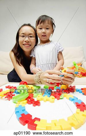 Stock Image - Mother and daughter looking at camera, toy pieces in front of them. Fotosearch