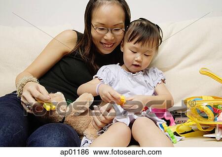 Stock Photograph - Mother and daughter on sofa, playing with toys. Fotosearch
