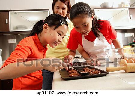 Stock Photo - Mother and two daughters in kitchen, baking. Fotosearch