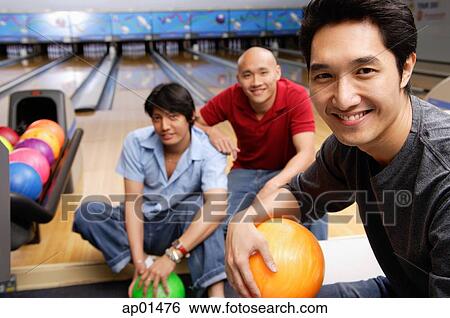 Stock Photograph - Three men in bowling alley, smiling at camera. Fotosearch