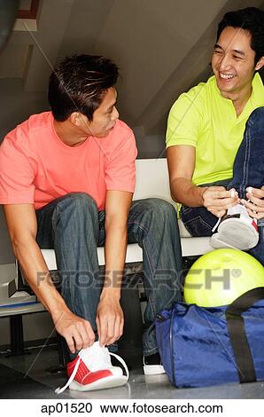 Stock Image - Two men in bowling alley, lacing up bowling shoes. Fotosearch