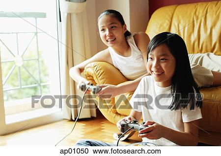 Stock Image - Two sisters in living room, playing video games. Fotosearch