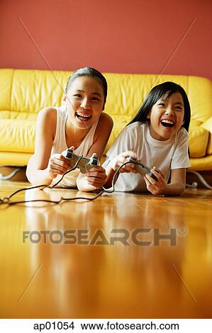 Two sisters lying on floor playing video games, smiling View Large Photo Image Picture - Two sisters lying on floor playing video games, smiling. Fotosearch