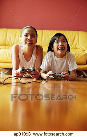 Two sisters lying on floor playing video games View Large Photo Image Stock Image - Two sisters lying on floor playing video games. Fotosearch