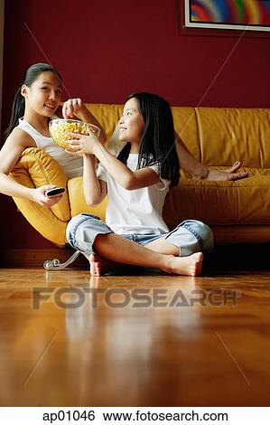 Two sisters sitting in living room, eating popcorn View Large Photo Image Stock Photograph - Two sisters sitting in living room, eating popcorn. Fotosearch