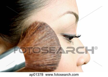 Stock Photo - Woman applying blusher with make-up brush, side view. Fotosearch