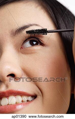 Stock Image - Woman applying mascara, close-up of face. Fotosearch
