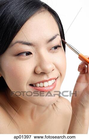 Stock Photo - Woman holding brush, applying eyeshadow, looking away. Fotosearch