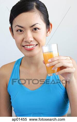 Stock Photography - Woman holding glass orange juice looking at camera. Fotosearch