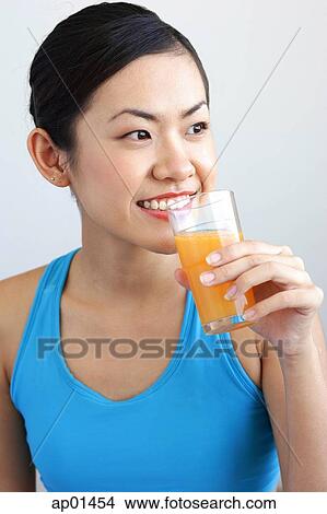 Picture - Woman holding glass orange juice to mouth, looking away. Fotosearch