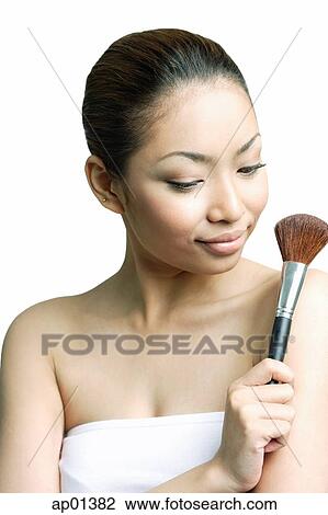 Stock Image - Woman holding make-up brush, looking away. Fotosearch