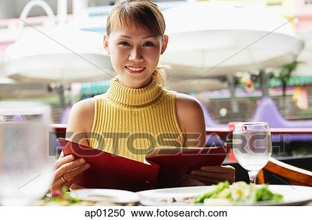 Stock Image - Woman holding menu, looking at camera, smiling. Fotosearch