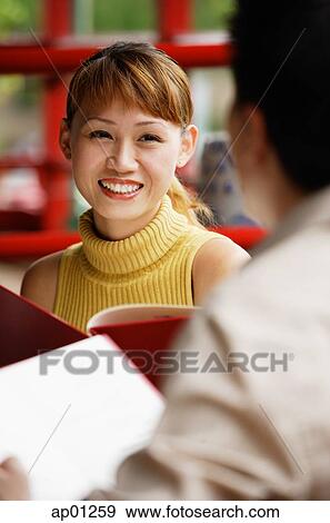 Woman holding menu, smiling, person in front of her, over the shoulder view View Large Photo Image Stock Photo - Woman holding menu, smiling, person in front of her, over the shoulder view. Fotosearch