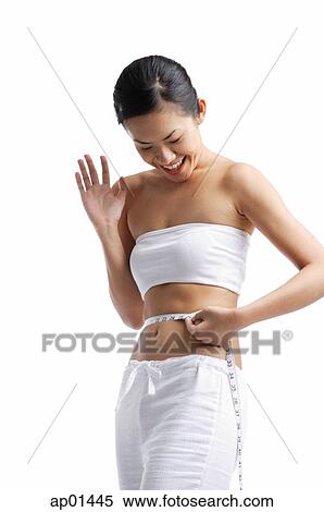 Woman holding tape measure around waist, looking down, smiling View Large Photo Image Stock Photography - Woman holding tape measure around waist, looking down, smiling. Fotosearch