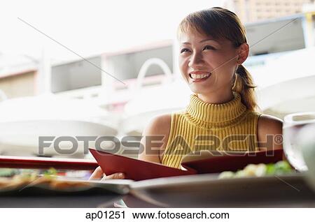 Stock Image - Woman in cafe, holding menu, looking away, low angle view. Fotosearch