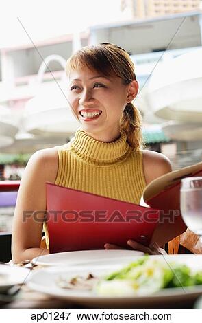 Woman in cafe, holding menu, looking away View Large Photo Image Stock Photo - Woman in cafe, holding menu, looking away. Fotosearch