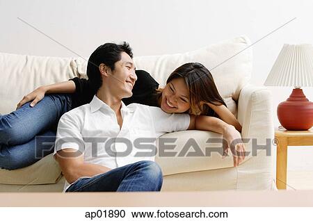 Stock Image - Woman lying on sofa, man sitting on floor in front of her, smiling. Fotosearch