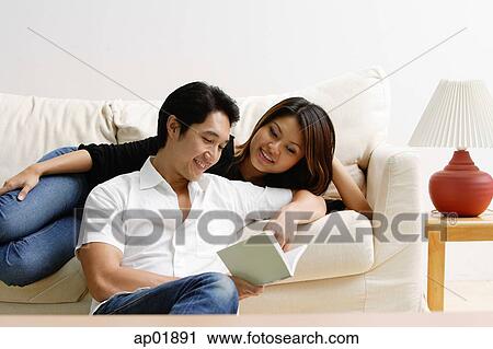 Woman lying on sofa, man sitting on floor in front of her, looking at book View Large Photo Image Stock Image - Woman lying on sofa, man sitting on floor in front of her, looking at book. Fotosearch