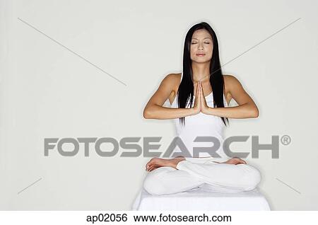 Stock Photograph - Woman practicing yoga, sitting in lotus position, hands together. Fotosearch